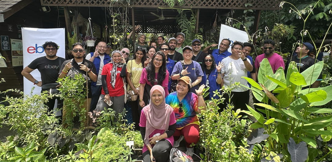 A group of eBay Changemakers smile in front of an assortment of greenery and plants.