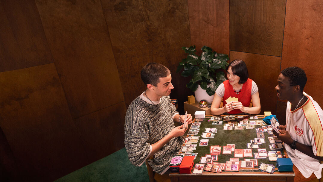 Three people gathered around a table playing a trading card game.