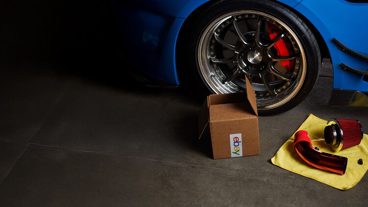 Automotive parts and tools beside a sports car wheel with an eBay shipping box.