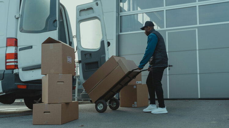Delivery worker loading cardboard boxes into a van.