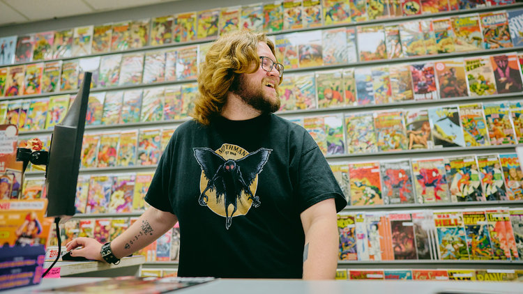 eBay seller working at a store counter with a wall of comic books on display in the background.