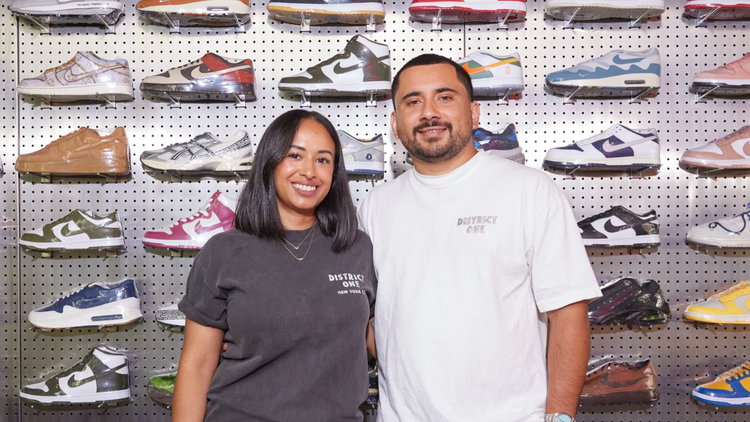 eBay sellers and owners of District One, Kristi Gonzalez and Daniel Arango, smile in front of a wall of sneakers.