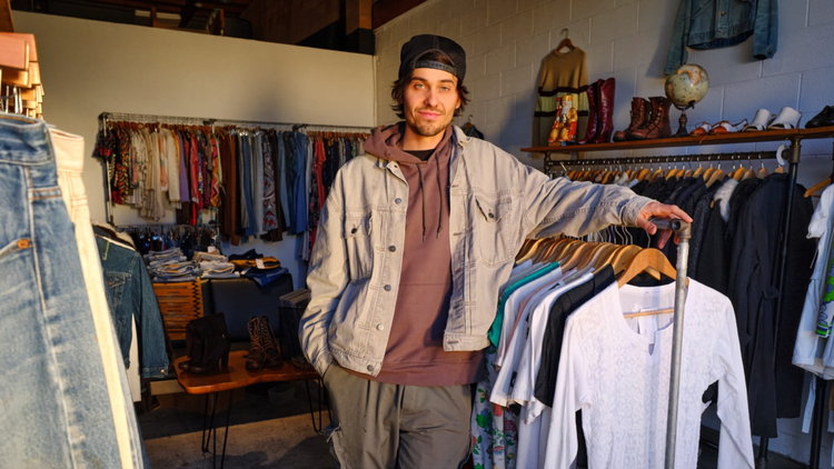 eBay seller poses with pre-loved fashion for sale inside his small business.